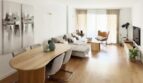 Sala de estar-comedor luminosa con suelo de madera, mesa de comedor ovalada, sofá gris y gran fachada de ventanas en Palma de Mallorca