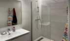 Moderno baño con ducha de cristal, ducha de lluvia, lavabo blanco y espejo grande en Palma de Mallorca