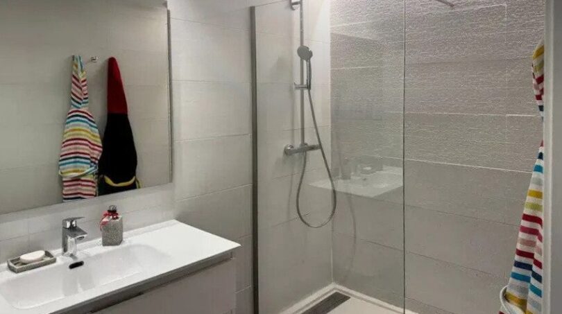 Moderno baño con ducha de cristal, ducha de lluvia, lavabo blanco y espejo grande en Palma de Mallorca