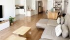 Sala de estar luminosa con sofá gris, suelo de madera y planta abierta con cocina y comedor en Palma