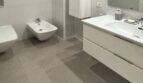 Baño moderno con inodoro suspendido, bidé, lavabo doble y grandes baldosas grises en vivienda urbana de Palma.