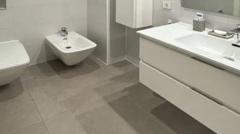 Baño moderno con inodoro suspendido, bidé, lavabo doble y grandes baldosas grises en vivienda urbana de Palma.