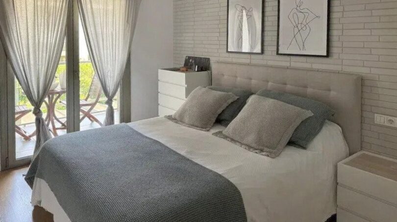 Dormitorio luminoso con cama doble, colcha gris, pared de ladrillo y acceso a balcón en Palma de Mallorca