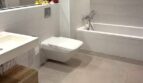 Baño moderno con bañera empotrada, inodoro suspendido, mueble inferior de madera y grandes baldosas de suelo en Palma de Mallorca.