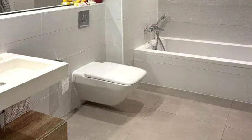 Baño moderno con bañera empotrada, inodoro suspendido, mueble inferior de madera y grandes baldosas de suelo en Palma de Mallorca.