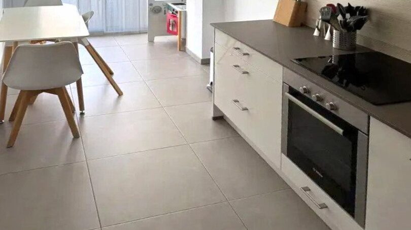 Sala de estar-comedor moderna con cocina empotrada blanca, placa de cocción, horno y suelo de baldosas claras en Palma