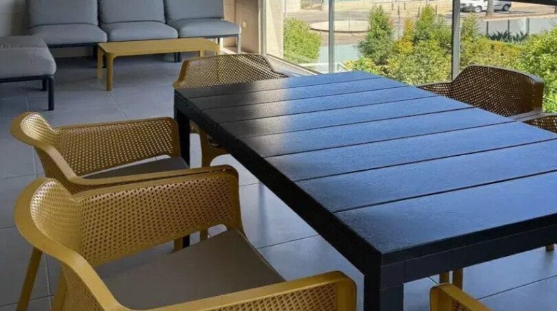 Balcón cubierto con mesa de comedor negra, sillas amarillas y área lounge con vistas a la ciudad en Palma