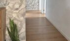 Luminoso pasillo con suelo de madera, papel pintado tropical, planta Sansevieria y cuadros enmarcados en apartamento Palma.