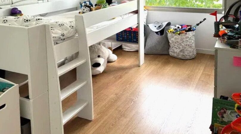 Habitación infantil con cama alta, suelo de madera, almacenamiento de juguetes y gran ventana con vistas al verde en Palma