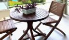 Balcón cubierto con muebles de madera, barandilla de vidrio y vista del jardín con piscina en Palma de Mallorca