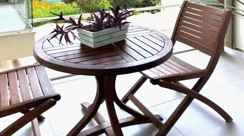Balcón cubierto con muebles de madera, barandilla de vidrio y vista del jardín con piscina en Palma de Mallorca