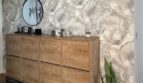Zona de entrada con cómoda de madera, espejo redondo, Sansevieria y papel tapiz con patrón tropical en Palma de Mallorca