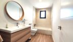 Modernes Badezimmer mit Holzwaschtisch, runden Spiegel, Badewanne und Holzboden in Einfamilienhaus Marratxí