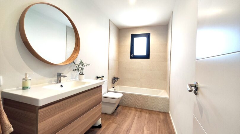 Modernes Badezimmer mit Holzwaschtisch, runden Spiegel, Badewanne und Holzboden in Einfamilienhaus Marratxí