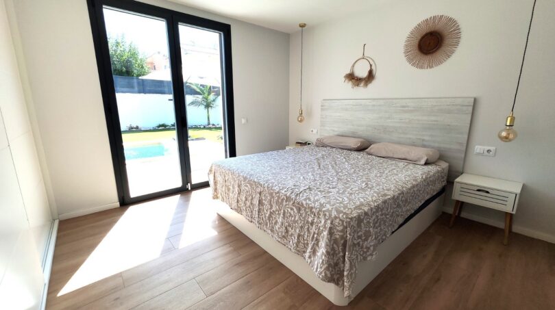 Helles Schlafzimmer mit Doppelbett, Holzboden und Glastür zum Pool in modernem Einfamilienhaus in Marratxí