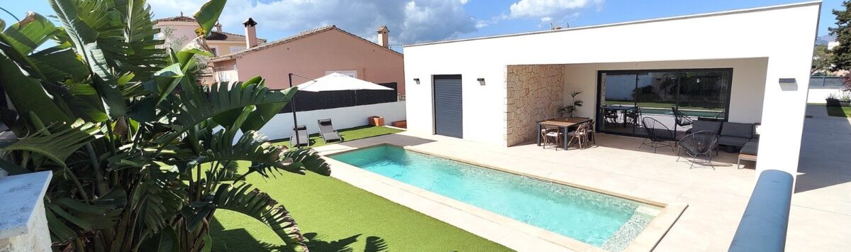 Modernes Einfamilienhaus in Marratxí mit rechteckigem Pool, Terrasse und tropischen Pflanzen unter blauem Himmel.