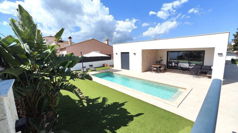 Modernes Einfamilienhaus in Marratxí mit rechteckigem Pool, Terrasse und tropischen Pflanzen unter blauem Himmel.