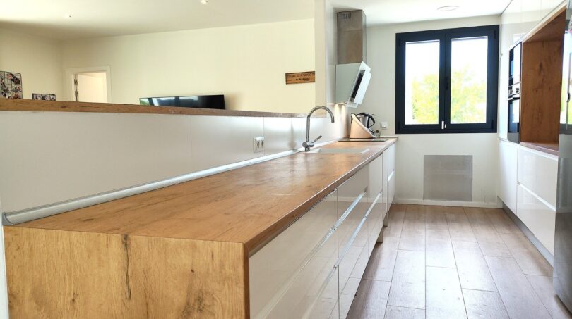 Moderne Küche mit Holzarbeitsplatte, weißen Fronten und großem Fenster im Einfamilienhaus Marratxí