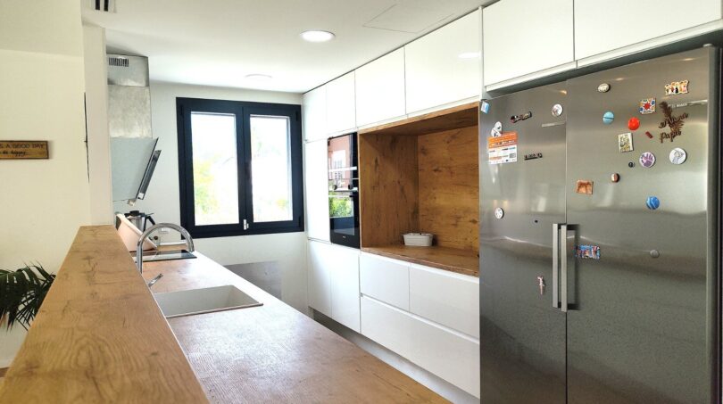 Moderne Küche mit Holztheke, weißen Hochglanzschränken und Edelstahl-Kühlschrank im Einfamilienhaus Marratxí