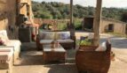 Überdachte Terrasse der Finca Artà mit Rattanmöbeln, Schattiernetz und Blick auf hügelige Waldlandschaft.