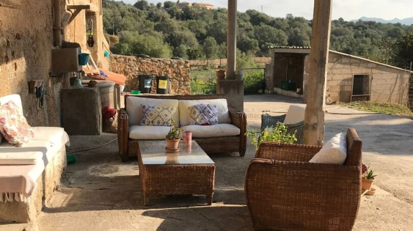 Überdachte Terrasse der Finca Artà mit Rattanmöbeln, Schattiernetz und Blick auf hügelige Waldlandschaft.