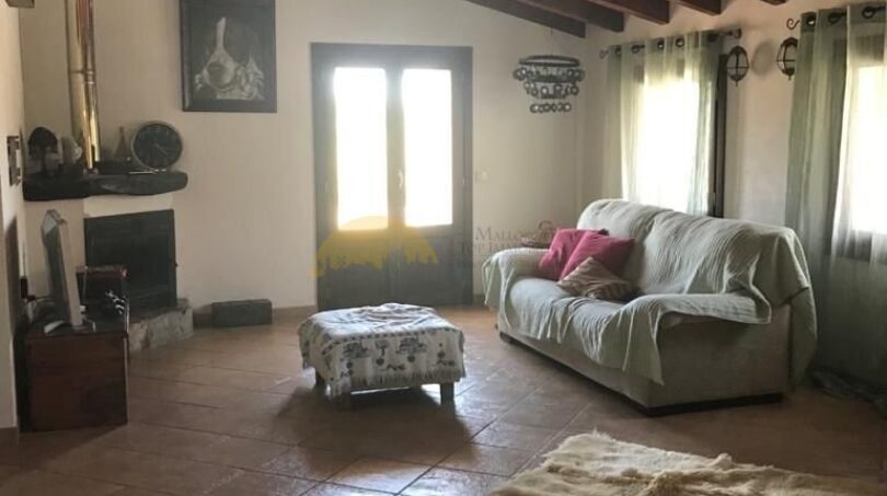 Rustikales Wohnzimmer der Finca in Artà mit Holzbalkendecke, Kamin und Natursteinboden