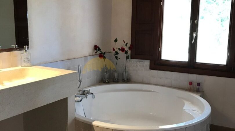 Luxuriöses Badezimmer der Finca in Artà mit runder Einbaubadewanne, Holzbalkendecke und Natursteinwaschbecken