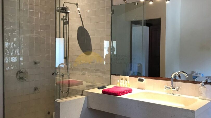 Modernes Badezimmer der Finca Artà mit Glasdusche, weißem Waschtisch und Holzbalkendecke