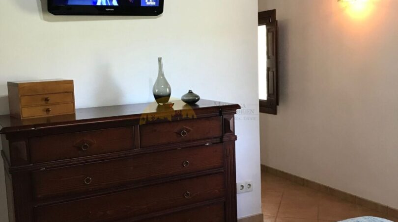 Schlafzimmer der Finca Artà mit Holzbalkendecke, antikem Kommode, WandTV und blauer Tagesdecke