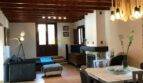 Rustikales Wohnzimmer der Finca Artà mit Holzbalkendecke, Kamin, blauer Couch und elegantem Esstisch.