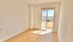 Helles, leeres Zimmer mit Holzboden, weißen Wänden und Balkontür mit Stadtblick in renovierter Wohnung, Palma