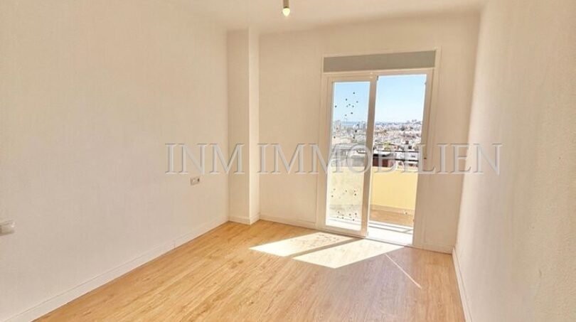 Helles, leeres Zimmer mit Holzboden, weißen Wänden und Balkontür mit Stadtblick in renovierter Wohnung, Palma