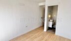 Helles, leeres Zimmer mit Laminatboden und Blick in modernes Bad mit Marmorfliesen in renovierter Wohnung.