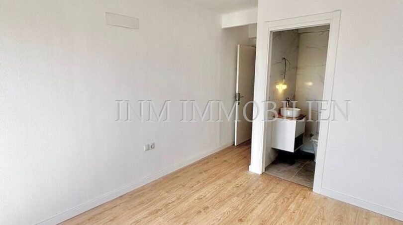 Helles, leeres Zimmer mit Laminatboden und Blick in modernes Bad mit Marmorfliesen in renovierter Wohnung.