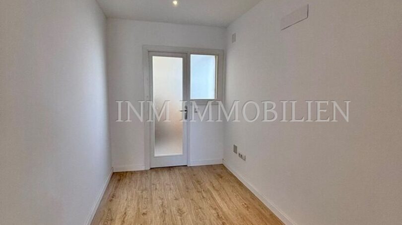 Leeres Zimmer mit Laminatboden, weißen Wänden, Einbauspot und Glastür in renovierter Wohnung, Palma de Mallorca.