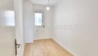 Helles, leeres Zimmer mit Laminatboden, weißen Wänden und kleinem Fenster in renovierter Wohnung, Palma