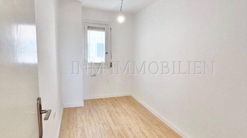 Helles, leeres Zimmer mit Laminatboden, weißen Wänden und kleinem Fenster in renovierter Wohnung, Palma