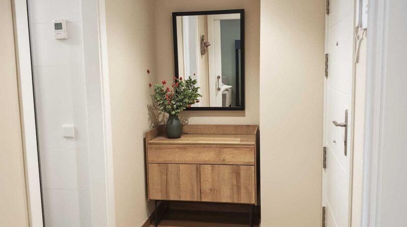 Heller Eingangsbereich mit Holzparkett, modernem Schuhschrank, Wandspiegel und Blumendekoration im Luxus-Apartment Palma