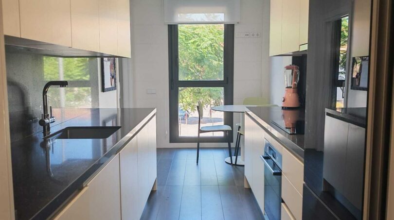 Moderne Galley-Küche mit weißen Hochglanzfronten, schwarzer Arbeitsplatte und Fensterfront in Luxus-Apartment Palma