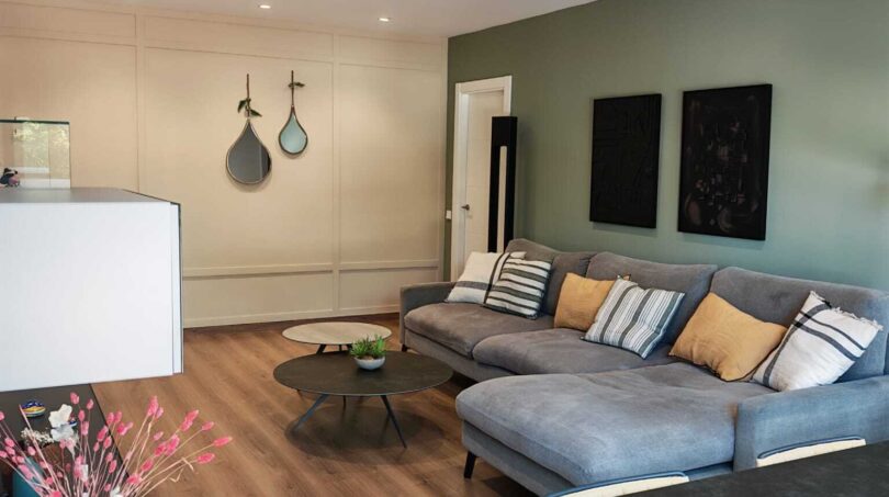Helles Wohnzimmer mit grauer Eckcouch, grüner Akzentwand und modernem Esstisch in Palma-Apartment