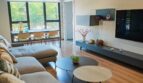 Helles Wohnzimmer mit grauem Sofa, Holzboden, TV-Wand und großen Fenstern mit Grünblick in Palma