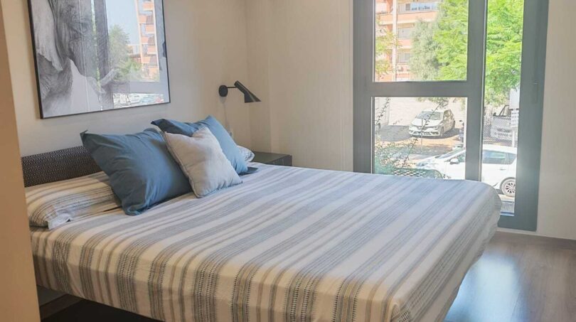 Helles Schlafzimmer mit Doppelbett, Holzboden, Deckenventilator und großem Fenster mit Stadtblick in Palma