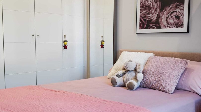 Helles Schlafzimmer mit rosa Bettwäsche, weißem Einbauschrank und Blumenkunstdruck in Luxus-Apartment Palma