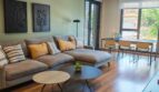 Helles Wohnzimmer mit grauer Couch, Holzboden, grüner Akzentwand und Zugang zur Terrasse in Palma de Mallorca
