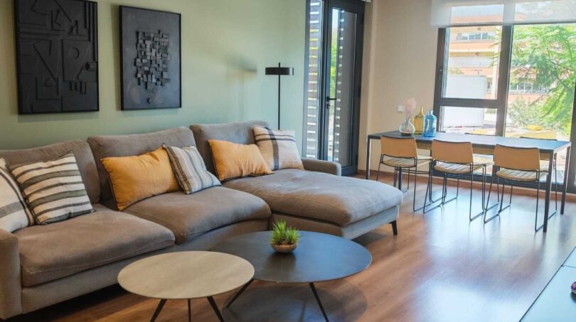 Helles Wohnzimmer mit grauer Couch, Holzboden, grüner Akzentwand und Zugang zur Terrasse in Palma de Mallorca
