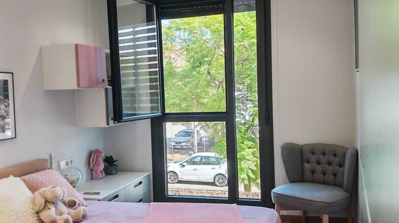 Helles Kinderzimmer mit rosa Bettwäsche, Deckenventilator und großem Fenster mit Grünblick in Palma-Apartment