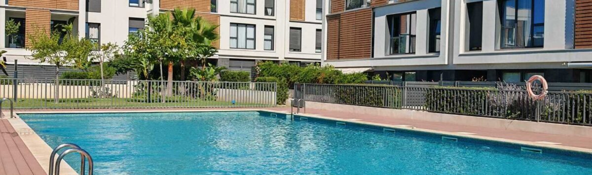 Gemeinschaftspool mit Holzterrasse der Luxusresidenz in Palma de Mallorca, umgeben von modernen Apartmentgebäuden.