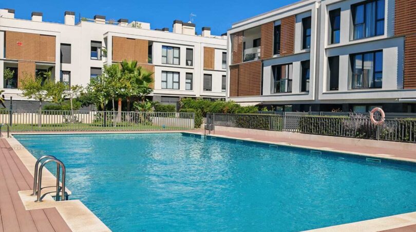 Gemeinschaftspool mit Holzterrasse der Luxusresidenz in Palma de Mallorca, umgeben von modernen Apartmentgebäuden.