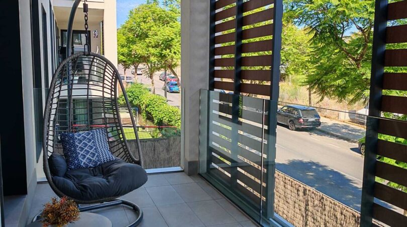 Moderner Balkon mit Hängesessel, Sichtschutz und Blick auf grüne Bäume in luxuriöser Residenz Palma