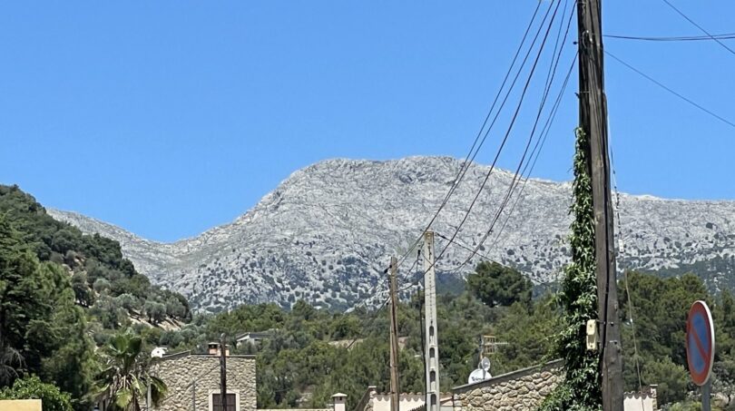 Vista de montaña rocosa con vegetación verde, muros de piedra natural y líneas eléctricas en Mancor de la Vall.
